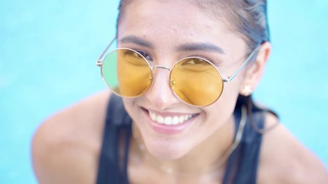 sexy beautiful girl in yellow glasses and a black  swimsuit resting on the edge of the pool, smiling and looking at the camera. slow motion ,close up view. Summer vacation holiday concept