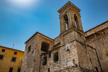 Fototapeta na wymiar Narni, Umbria, Italy - The medieval cathedral of San Giovenaleo in the ancient village of Narni. The side with the bell tower and the church clock. The blue sky in the summer.
