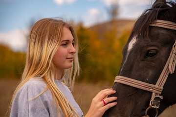 Obraz premium A young girl with blond hair gently strokes the brown horse's muzzle.
