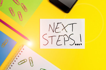 Writing note showing Next Steps. Business concept for something you do after you have finished doing first one Paper sheets square notebook pencil clips smartphone colored background