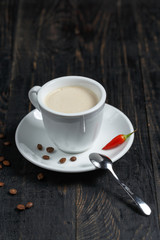 Cup of aromatic coffee on a black wooden table with coffee beans and jalopeno pepper
