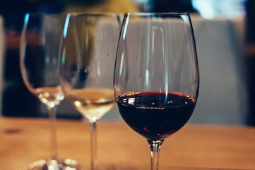 Close up image of three glasses with red and white wine, on wooden table, served for wine tasting event. Blurred background. Bar or restaurant interior, subdued light. Selective focus, film grain effe