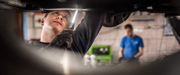 Obraz na płótnie Canvas Auto mechanic repairer checking condition under car on vehicle lift
