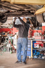 Auto mechanic repairer checking condition under car on vehicle lift