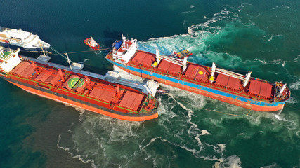 Aerial drone photo of tug boats manoeuvring industrial bulk carrier by pushing or pulling in...