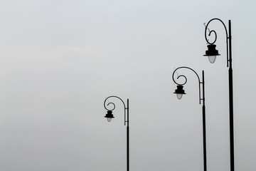 Three metal street lamps on a sky background. It looks like a family. Father, mother and child.