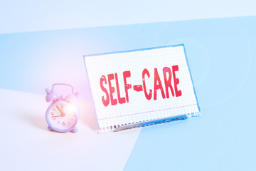 Word writing text Self Care. Business photo showcasing practice of taking action to preserve or improve ones own health Mini size alarm clock beside a Paper sheet placed tilted on pastel backdrop