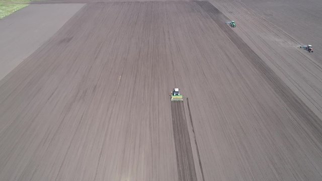 Flying on a copter over a gray field with 4 working tractors. Aerial view
