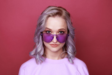 Portrait of young woman in bright glasses standing isolated over the pink background