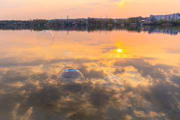 Fototapeta na wymiar Soap bubbles and evening sunset reflextion in river or lake