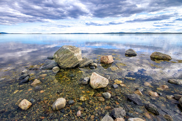 Stones on the shore of the Kandalaksha Bay of the White Sea. Clouds and sky reflected in water