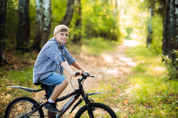 Little Caucasian boy stands leaning on the bike posing for the camera. Teenager ready to ride bicycle in park on summer day. Weekend activity.