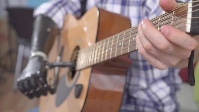 young man with a prosthetic arm plays an acoustic guitar close up