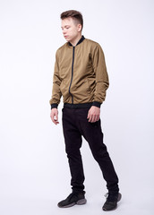 Young man in jeans, shiny nylon gold bomber jacket on white background.