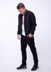 Young man in jeans, black bomber jacket on white background.