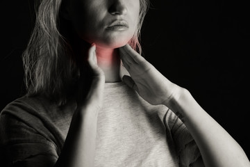 Female checking thyroid gland by herself. Close up of woman in white t- shirt touching neck with...