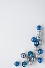 Scattered silver and blue little baubles arranged as a frame on white background. Vertical minimalistic greeting card for Christmas. Copy space for wishes.
