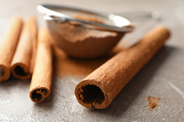 Cinnamon sticks, powder and sieve on grey background, space for text
