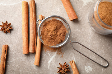 Obraz na płótnie Canvas Cinnamon sticks, powder and sieve on grey background, top view