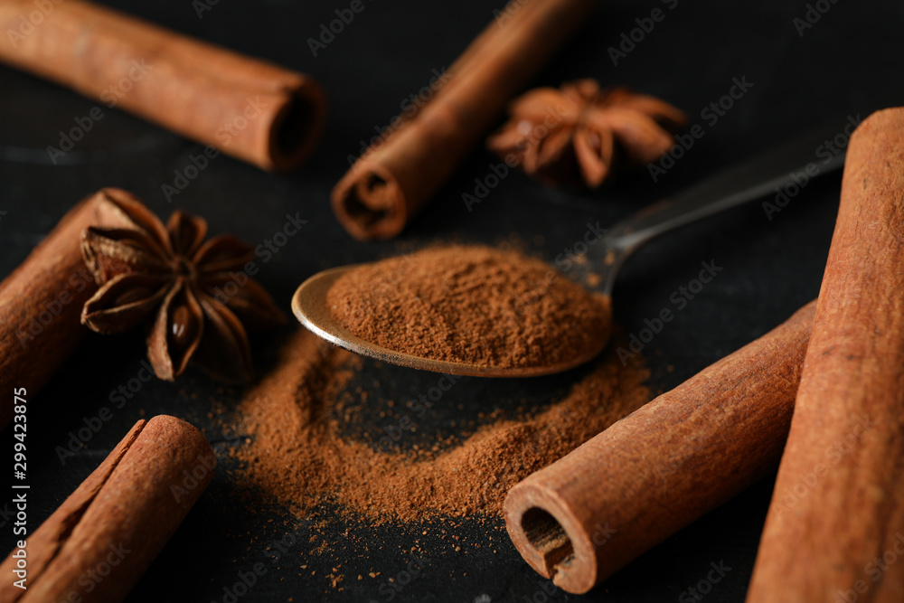 Wall mural Cinnamon sticks, anise and spoon on black background, space for text