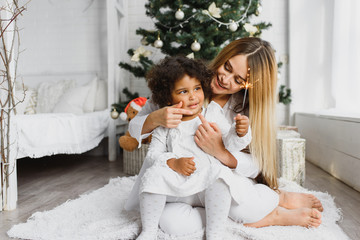 Fototapeta na wymiar Merry Christmas and Happy Holidays! Cheerful mom and her cute daughter at Christmas tree. Parent and little child having fun near Christmas tree indoors. Loving family with presents in room.