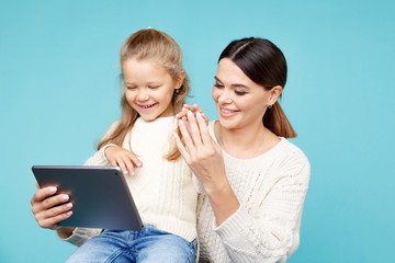 Portrait of mother and daughter with tablet sitting on the floor isolated over the blue studio