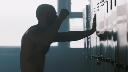 Silhouette of young sportsman hitting locker in gym room dealing with motivation crisis stress after competition failure