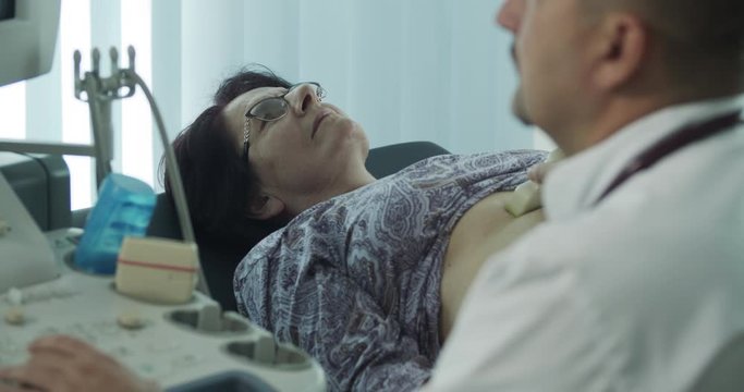 Portrait of mature doctor while examining senior female patient on ultrasound machine in the office room.