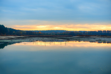 Gloomy morning: sunrise and dark blue skies on half-dry lake, panoramic image