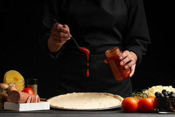 The chef cooks Italian pizza, topping with sauce. Freeze in the air. Against the background of...
