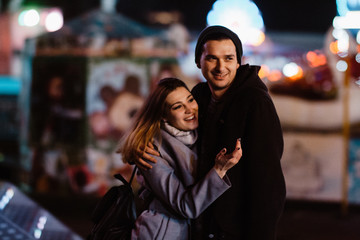 Photo of a smiling loving couple walking outdoors in amusement park having fun hugging in the evening