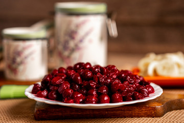 Full plate sour cherries on a chopping board,container jars, banana slices and a basting brush