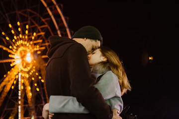 Fototapeta premium Photo of a smiling loving couple walking outdoors in amusement park having fun hugging in the evening