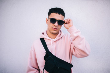 Obraz premium City portrait of handsome hipster guy wearing pink blank hoodie with waist black bag with space for your logo or design. Mockup for print