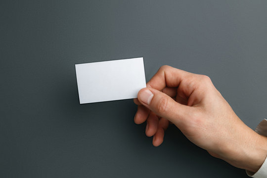 Male hand holding a blank business card on grey background for text or design. Blank credit card templates for contact or use in business. Finance, office. Mock up. Copyspace.