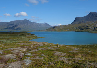 Lapland nature landscape with blue glacial lake Allesjok near Alesjaure, birch tree forest, snow capped mountains. Northern Sweden, at Kungsleden hiking trail. Summer sunny day