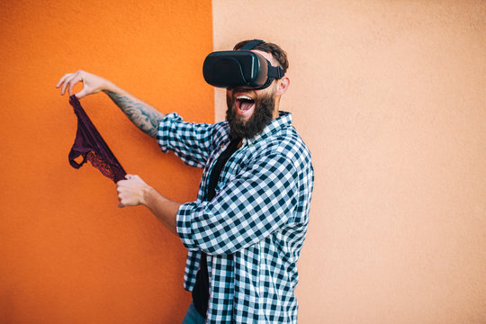 Virtual sex concept. Man in VR glasses play cybersex games and holding female panties in his hands.