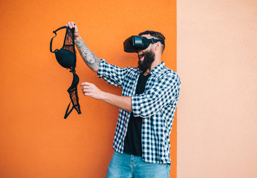 Virtual sex concept. Man in VR glasses play cybersex games and holding a female bra in his hands.