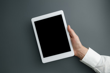 Male hand holding tablet with empty screen on grey background for text or design. Blank gadget templates for contact or use in business. Finance, office, purchases. Mock up. Copyspace.
