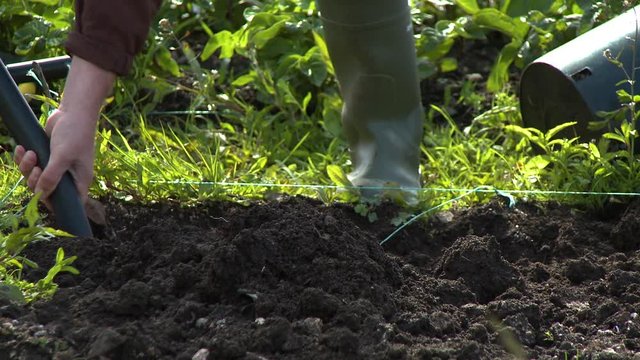Close up of a person using a shovel to till rich, dark soil in a small garden