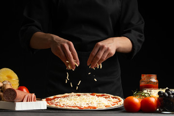 Chef cooks pizza, sprinkled with mozzarella cheese, freezing in motion on the background with ingredients. Recipe book, menu, home cooking