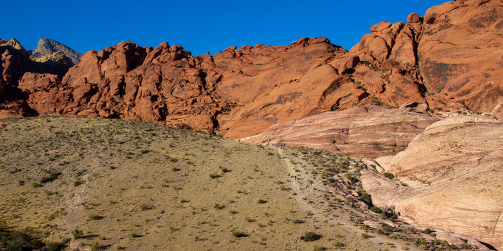 Hikers on a trail at the base of Aztec Sandstone cliffs of Red Rock Canyon in Nevada