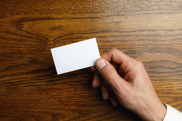 Obraz premium Male hand holding a blank business card on wooden background for text or design. Blank credit card templates for contact or use in business. Finance, office. Mock up. Copyspace.