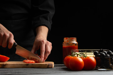 Chef cooks pizza, slices fresh tomatoes, on the background with ingredients. Recipe book, menu,...