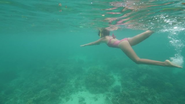 Underwater view of a sexy woman in a pink swimsuit swimming in the blue ocean.