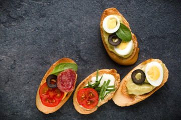 Open faced sandwich canape or crostini on dark stone background closeup. Top view.