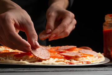 The chef cooks pizza, spreads salami on the background with ingredients. Recipe book, menu, home cooking. Close up macro