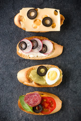 Open faced sandwich canape or crostini on dark stone background closeup. Top view.