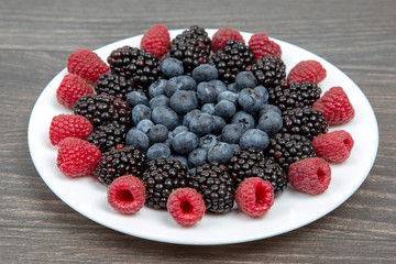 raspberries, blueberries and blackberries on a white plate. Vitamin and Diet Food