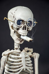 close up of skeleton wearing glasses smoking a cigarette on black background
